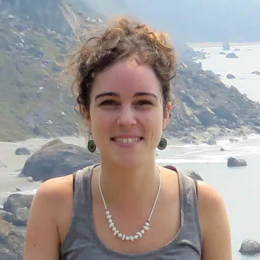 Cristina Romera Castillo stands for a picture, smiling, in front of the ocean and a mountain cliffside.