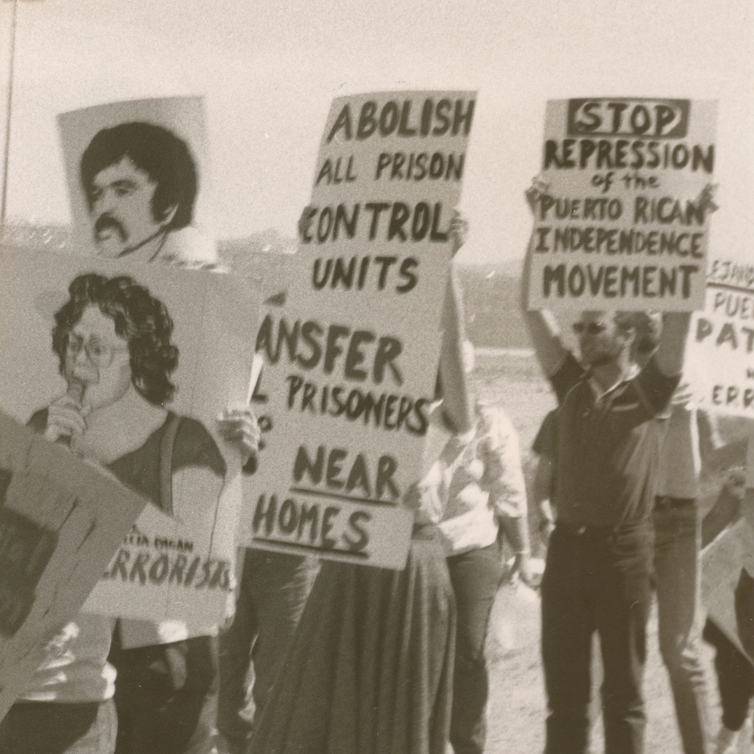Black and white photo of Puerto Rican activists with signs about the Puerto Rican Independence Movement and the abolishment of prison control units