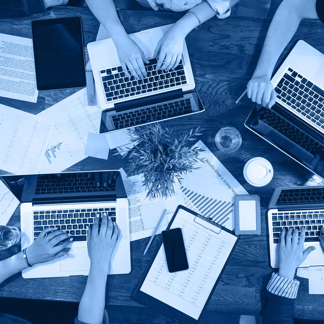 A bird's eye shot of four people working on their laptops, surrounded by business documents.