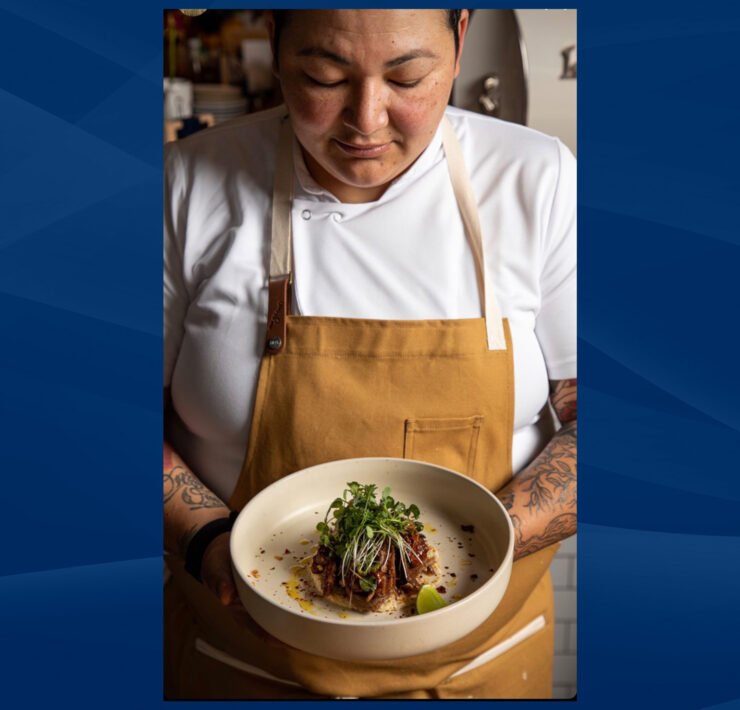 Headshot of Chef Melissa Araujo where she wears an old gold apron and looks down at a bowl of one of her culinary creations.