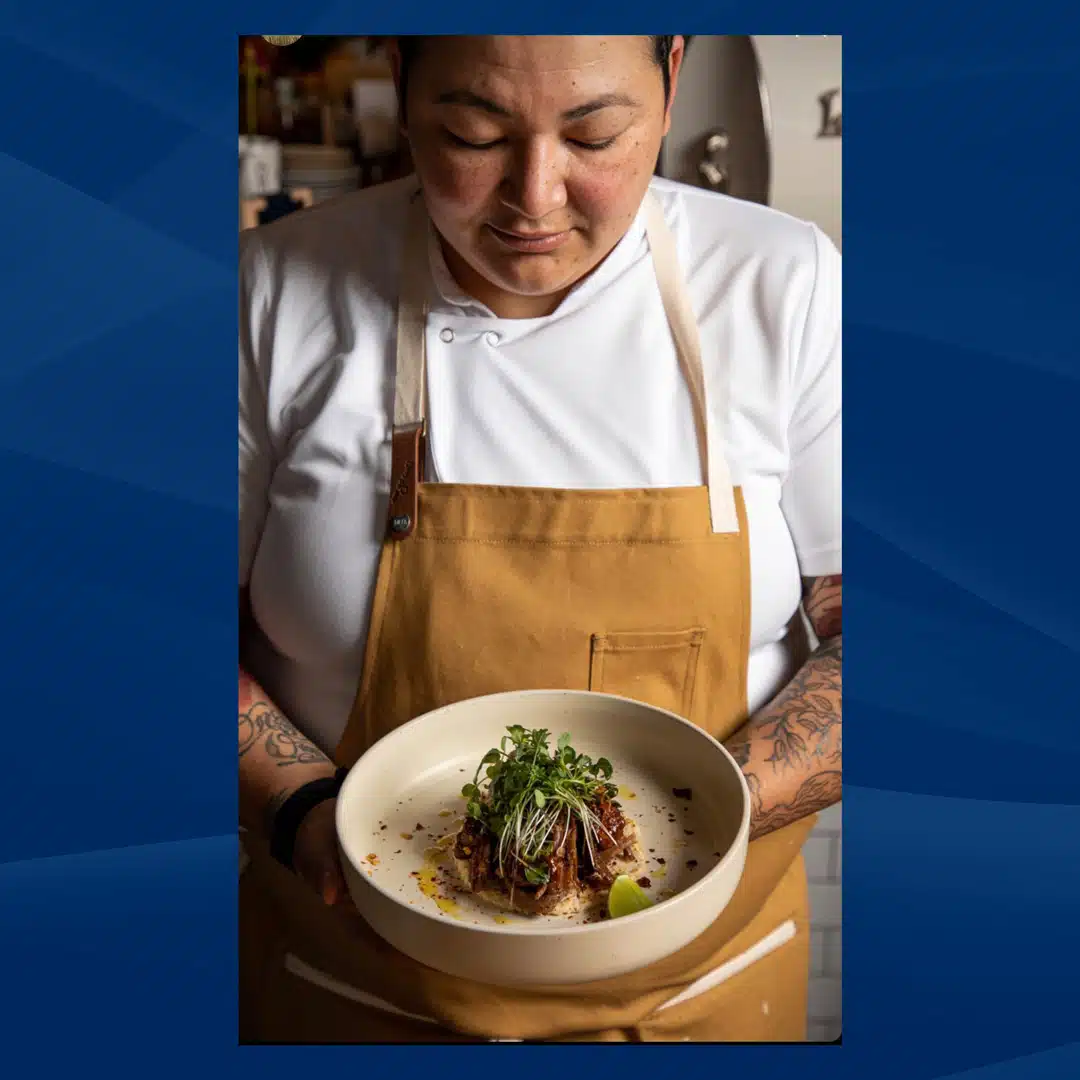 Headshot of Chef Melissa Araujo where she wears an old gold apron and looks down at a bowl of one of her culinary creations.