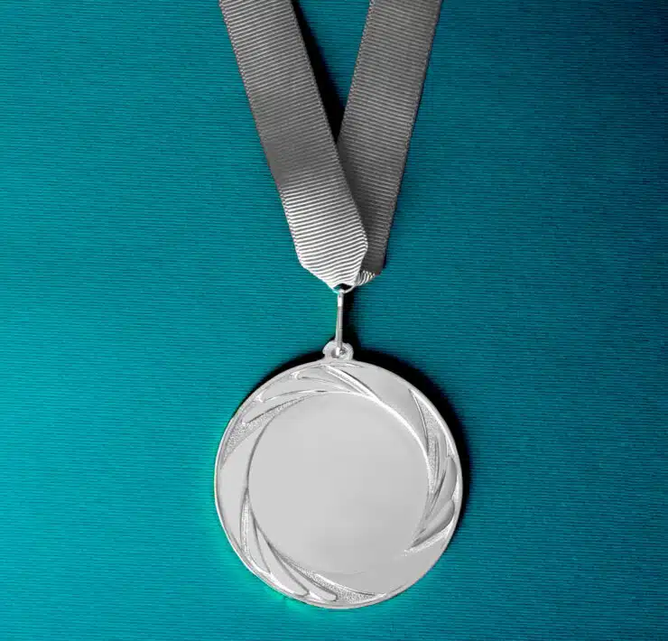 A silver medal lays flat on a teal background