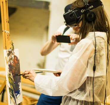 A woman wears a VR Oculus headset while painting on a canvas