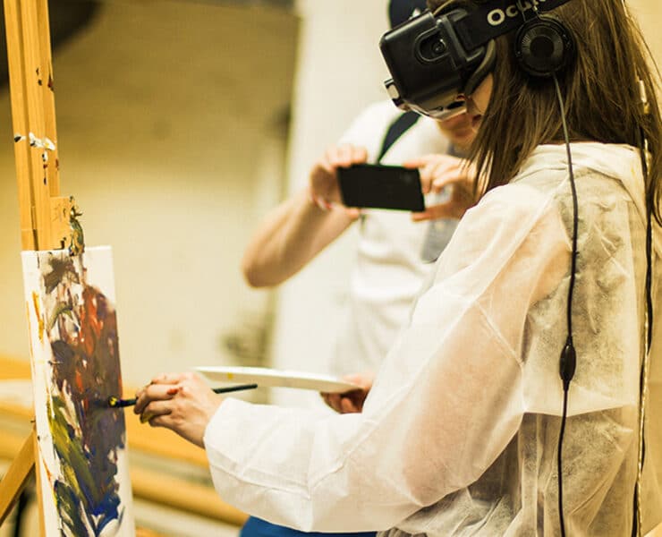 A woman wears a VR Oculus headset while painting on a canvas