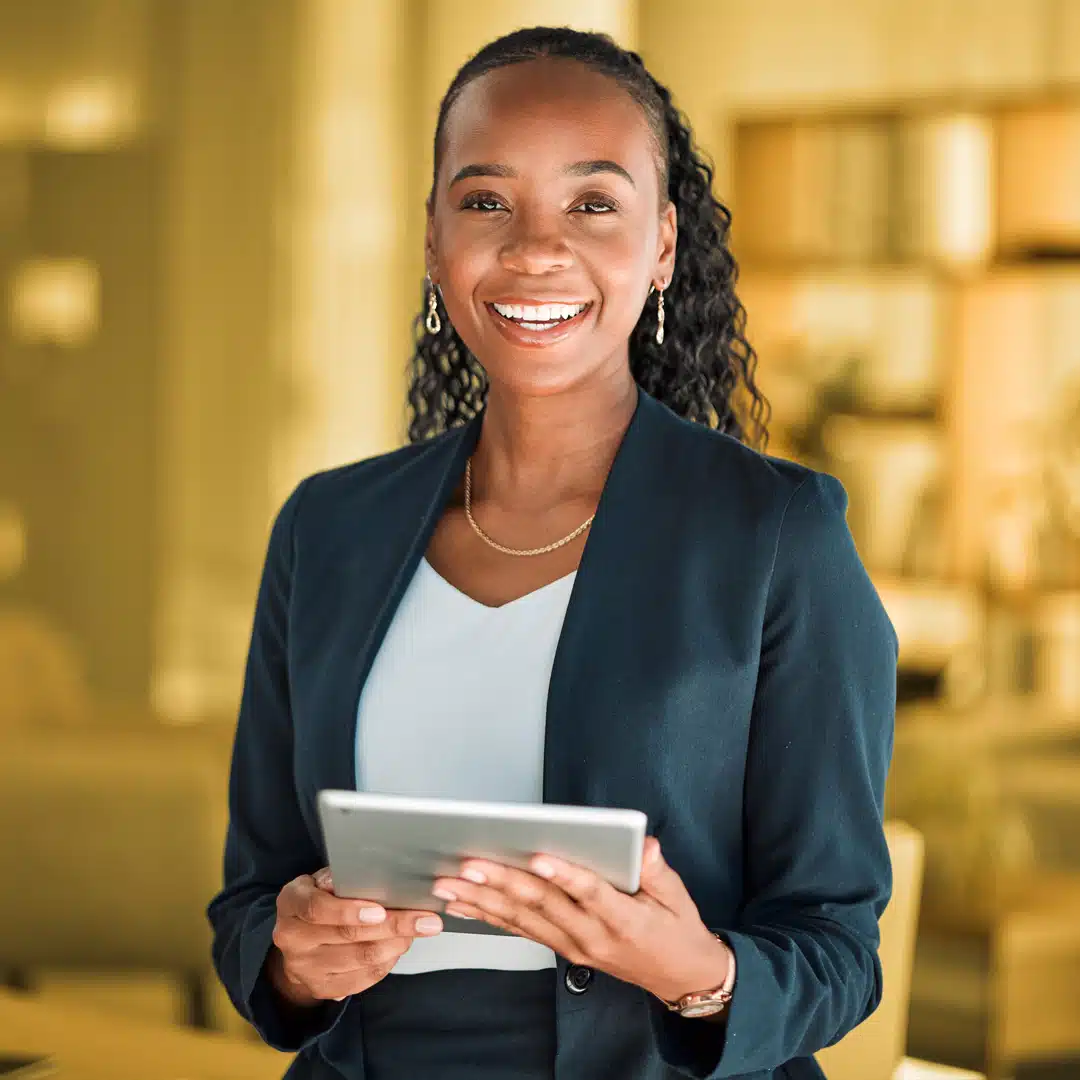 A headshot of a woman of color holding a tablet and smiling at the camera with a yellow background