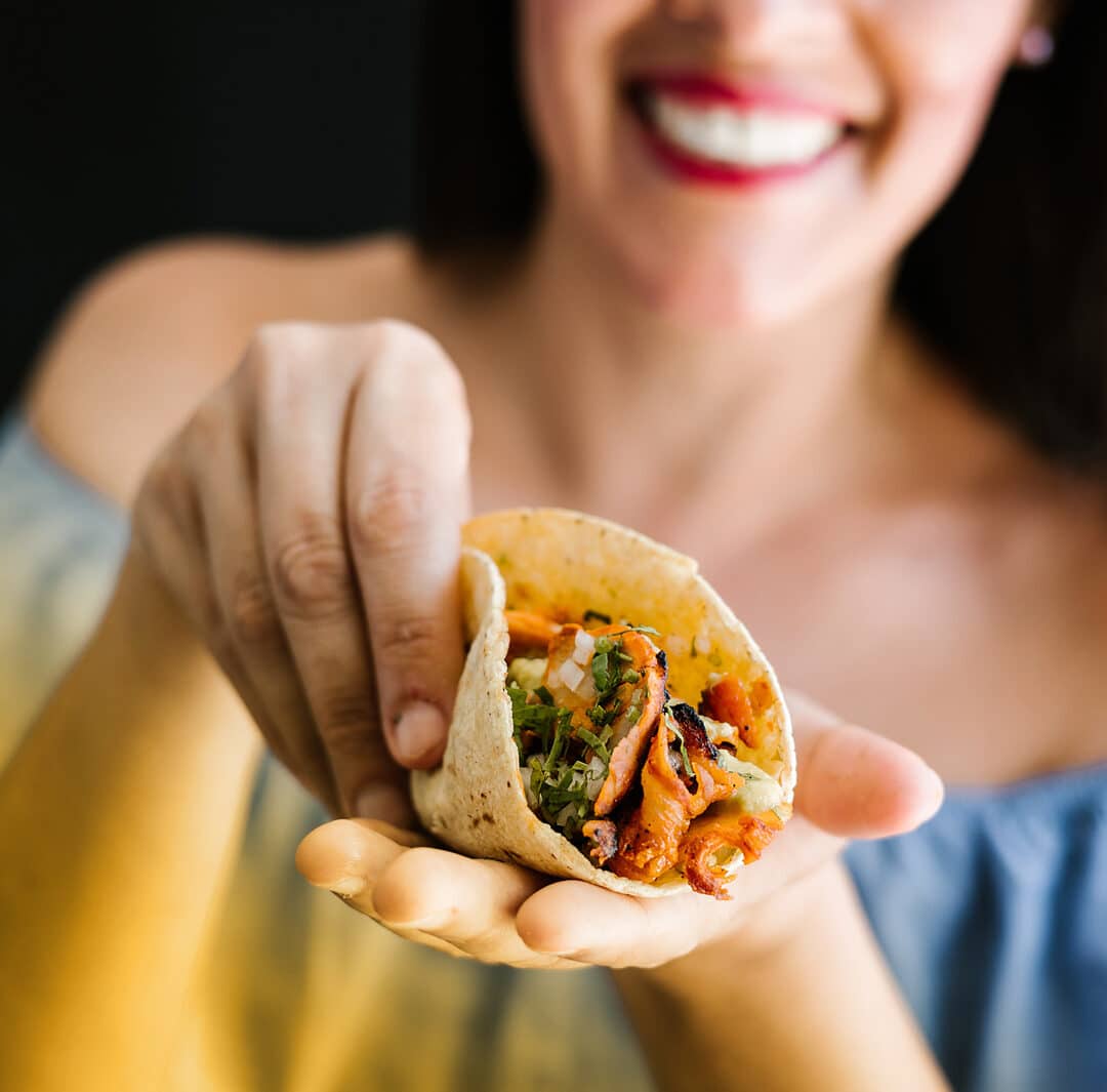 A woman cups an al pastor taco in her hands