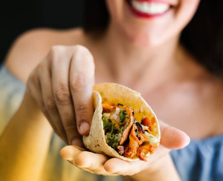 A woman cups an al pastor taco in her hands