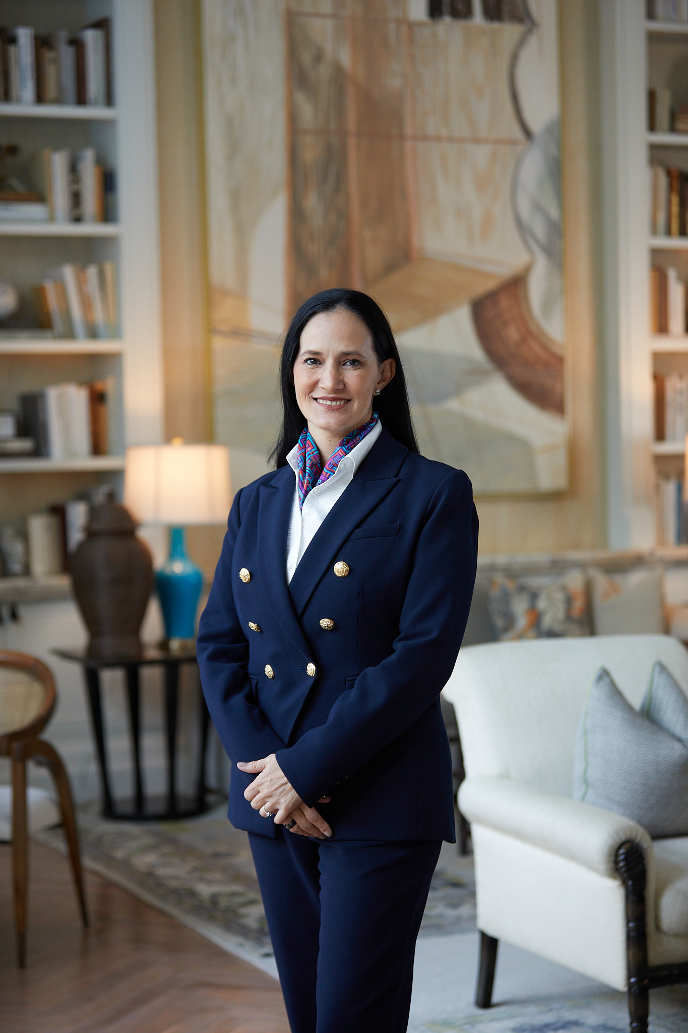 A portrait shot of Monica Ortiz, managing director of Rosewood Baha Mar resorts, wearing a dark blue suit with gold buttons and a colorful multicolor collar/scarf in the lobby of the resort