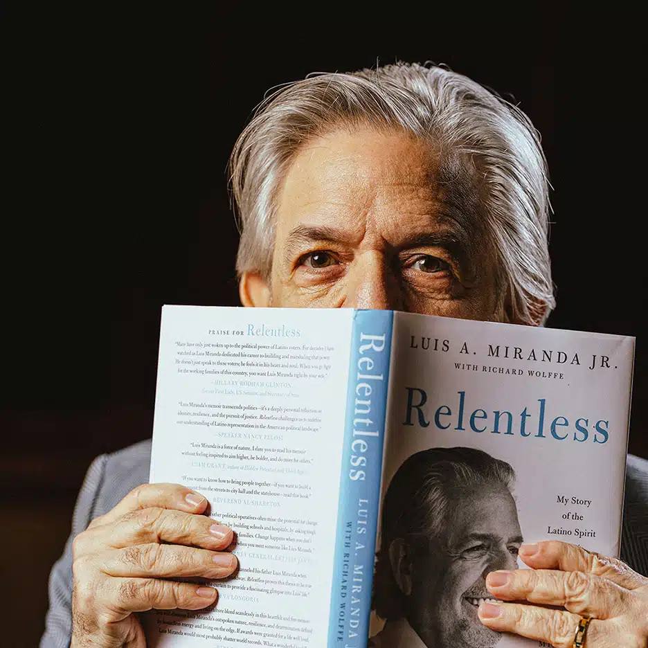 Luis A. Miranda Jr. holds his memoir Relentless open with the cover facing out, and the book is cover all but his eyes and the top of his head